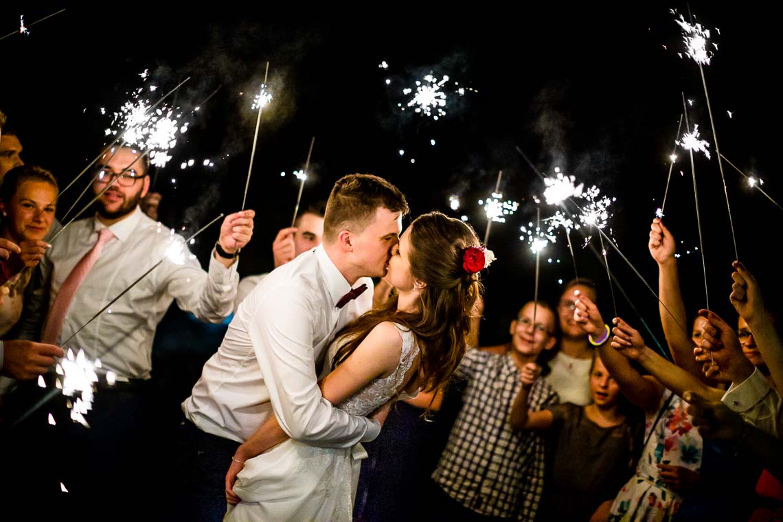 Fotograf ślubny Wrocław. Zimne ognie na weselu. Zdjęcia z zimnymi ogniami podczas wesela. Para Młoda w otoczeniu gości weselnych z zimnymi ogniami w rękach.